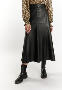 Zwarte leren midi-rok met knopen aan de voorkant, A-lijnvorm, gladde textuur, gecombineerd met zwarte enkellaarsjes met stevige zolen.