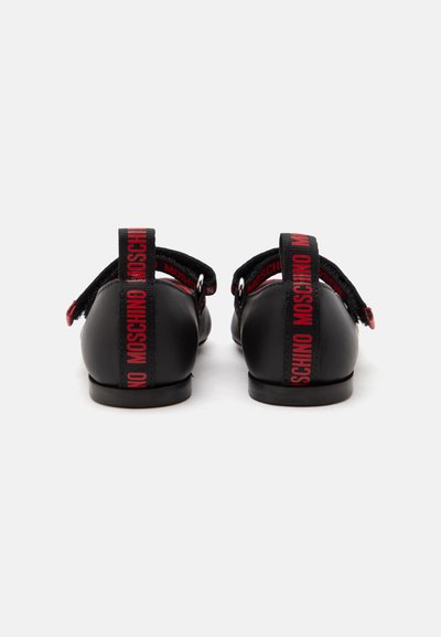 Paire de chaussures plates noires avec le logo rouge "MOSCHINO" sur les languettes arrière et des brides réglables à la cheville, vues de dos.
