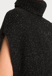 Poncho nero in maglia con colletto alto, caratterizzato da un motivo testurizzato e fili metallici intrecciati. Sides aperti per una maggiore ventilazione.