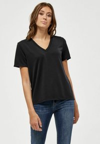 Schwarzes V-Ausschnitt-T-Shirt, kurze Ärmel, weicher Stoff, lässige Passform, glatte Textur, getragen mit blauen Jeans, vor einem hellgrauen Hintergrund.