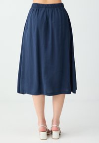 Jupe bleu marine longueur genou avec taille élastique portée avec des sandales blanches à talons blocs, vue de dos.