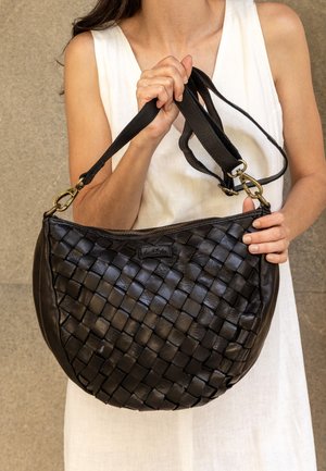 Bolso de mano de cuero negro trenzado con forma redondeada, que cuenta con cierre de cremallera y correa de tela ajustable. Detalles en hardware dorado.
