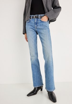 Lyseblå, højtaljede jeans med en lige ben-design. Bæres med et sort bælte med cirkulære huller og sorte støvler med hæl.