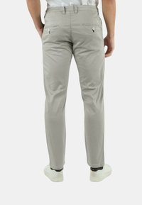 Pantaloni grigi slim-fit con tasche posteriori a bottone e una texture liscia, abbinati a sneakers bianche e una camicia infilata.