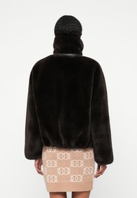 Casaco de pelagem sintética castanho-escuro com um colarinho alto e corte solto, apresentando uma cintura ajustada e um mínimo de costura.