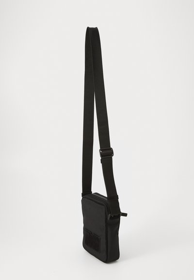 Svart tyg crossbody-väska med justerbart band, rektangulär form, dragkedjestängning och framficka. Slät textur.