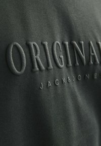 Donkergroene sweatshirt met reliëfletters "ORIGINAL" boven "JACK&JONES," met een textuur en zachte stofafwerking.