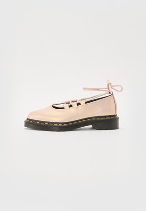 Zapato plano de cuero rosa claro con suela negra, costuras amarillas, lados abiertos, diseño con cordones y atadura en el tobillo sobre fondo liso.