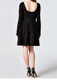 Svart spetsklänning med lång ärm och en låg rundad rygg. Utsvängd kjol med ett texturerat blommönster. Bärs med svarta högklackade skor.