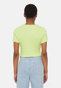 Avskuren, kortärmad skjorta i ljus limegrön ribbad tyg. Har en rund halsringning och en åtsittande design, som matchas med ljusblå jeans.