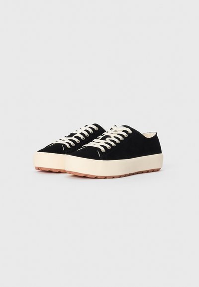 Mustad suede tossud valgete paeltega, ümarate ninade, paksu kreemja tallaga ja tekstuuriga kummist välispinnaga. Ilma nähtavate logode või keerukate mustriteta.