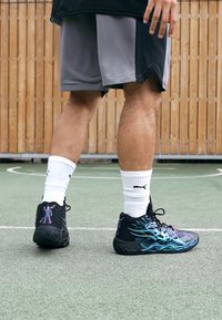 Sorte træningssko med blåt flamme design og lilla detaljer, parret med hvide ankelsokker. Grå shorts og en sort top bæres.