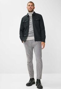 Giacca grigio scuro con due tasche sul petto, indossata sopra un maglione grigio chiaro a fantasia. I pantaloni grigi chiari e le scarpe nere stringate completano il look.