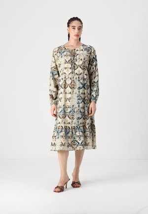 Robe à manches longues, à hauteur des genoux, de couleur beige avec des motifs floraux bleus et bruns. Présente une taille froncée et un détail à nouer au niveau du col.