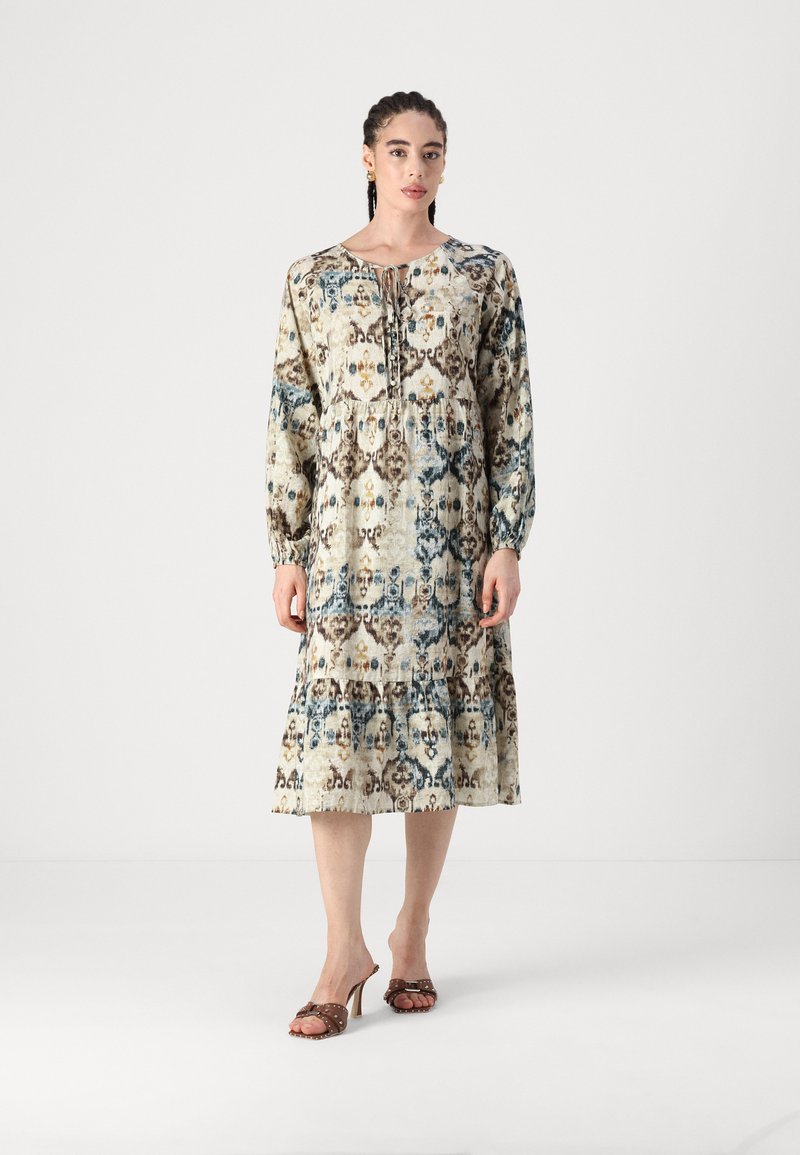 Μακρυμάνικο, μέχρι το γόνατο φόρεμα σε μπεζ χρώμα με μπλε και καφέ λουλουδάτα μοτίβα. Διαθέτει συγκεντρωμένη μέση και λεπτομέρεια με κορδόνι στον λαιμό.