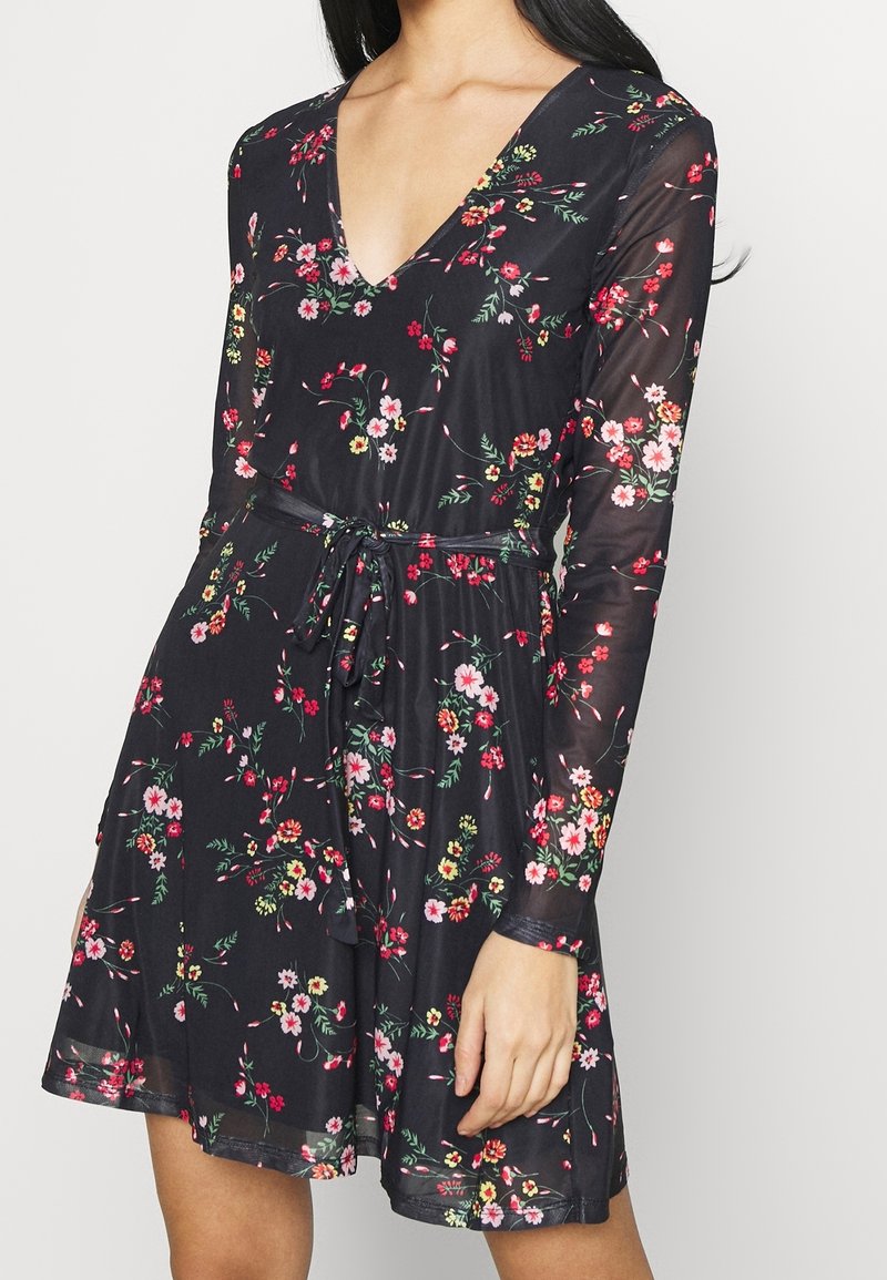 Schwarzes Blumenkleid mit langen Ärmeln, V-Ausschnitt und Bindegürtel. Es zeigt ein Muster aus Rosen und grünen Blättern auf einem durchsichtigen Stoff.