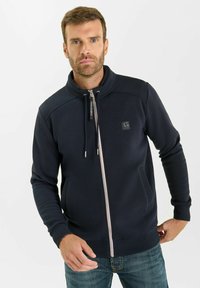 Felpa con zip color navy, colletto alto, tasche frontali e strisce bianche sullo zip; realizzata in un tessuto morbido e testurizzato.