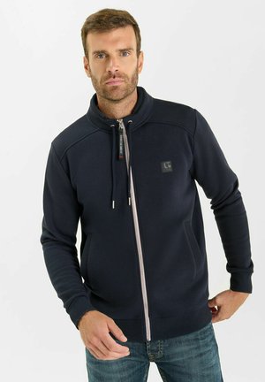 Felpa con zip color navy, colletto alto, tasche frontali e strisce bianche sullo zip; realizzata in un tessuto morbido e testurizzato.