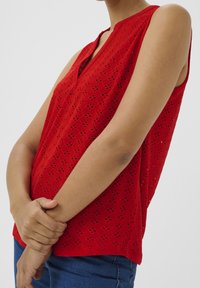 Top rosso senza maniche con scollo a V, caratterizzato da un motivo a reticolo e piccole aperture. Realizzato in tessuto leggero, offre una vestibilità comoda.