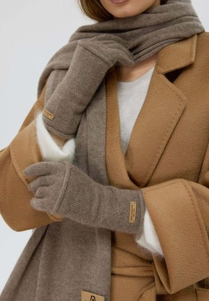 Braune Strickhandschuhe mit Fingeröffnungen und einem Lederetikett; kombiniert mit einem passenden braunen und beigen Schal und einem beigefarbenen Wollmantel.