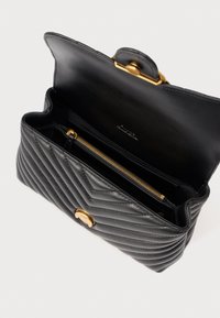 Μαύρη δερμάτινη τσάντα χειρός με σχεδιασμό καπιτονέ, χρυσό κούμπωμα και εσωτερική τσέπη με φερμουάρ. Υφή εξωτερικά, ανοίγει σε έναν ευρύχωρο κύριο χώρο.