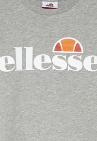 Pelēka kokvilnas T-kreklu ar lielu baltu "ellesse" logotipu un oranžu un sarkanu pusi apļa dizainu virs teksta.