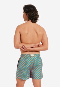 Badeshorts mit einem geometrischen Muster in Orange und Türkis, elastischem Bund und Seitentaschen; leichtes Material, designed für Komfort und Bewegungsfreiheit.
