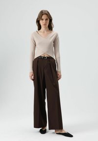 Beige geribbelde longsleeve met een gekruiste voorkant, gecombineerd met hooggetailleerde brede bruine broek en zwarte instapschoenen.