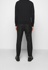 Suéter negro de cuello redondo y puños acanalados, combinado con pantalones negros de pierna recta. Diseño sencillo y textura suave.