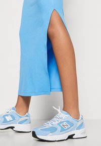 Light blue ribbed dress with side slits, paired with light blue New Balance sneakers featuring mesh and suede accents, detailed laces, and logo.