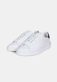 Sneakers bianchi in pelle con lacci piatti, punta rotonda e un tallone a contrasto nero. Superficie strutturata, design minimalista.