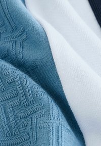 Textil med en ljusblå texturerad sektion med präglade mönster, i kontrast till solid vit och mörkblåa områden.