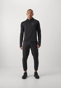 Zwarte atletische top met lange mouwen en een ritssluiting tot een kwart, met bijpassende taps toelopende broek. Gemaakt van ademend materiaal met een nauwsluitend silhouet.