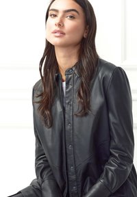 Sort læderjakke med skjorteudsnit og knaplukning med trykknapper, med lange ærmer og en glat finish.