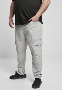 Hellgraue Cargo-Hosen mit entspannter Passform, die Seitentaschen haben und eine Textur aufweisen, die auf ein leichtes, atmungsaktives Gewebe hinweist. Schwarze Sneakers sind getragen.