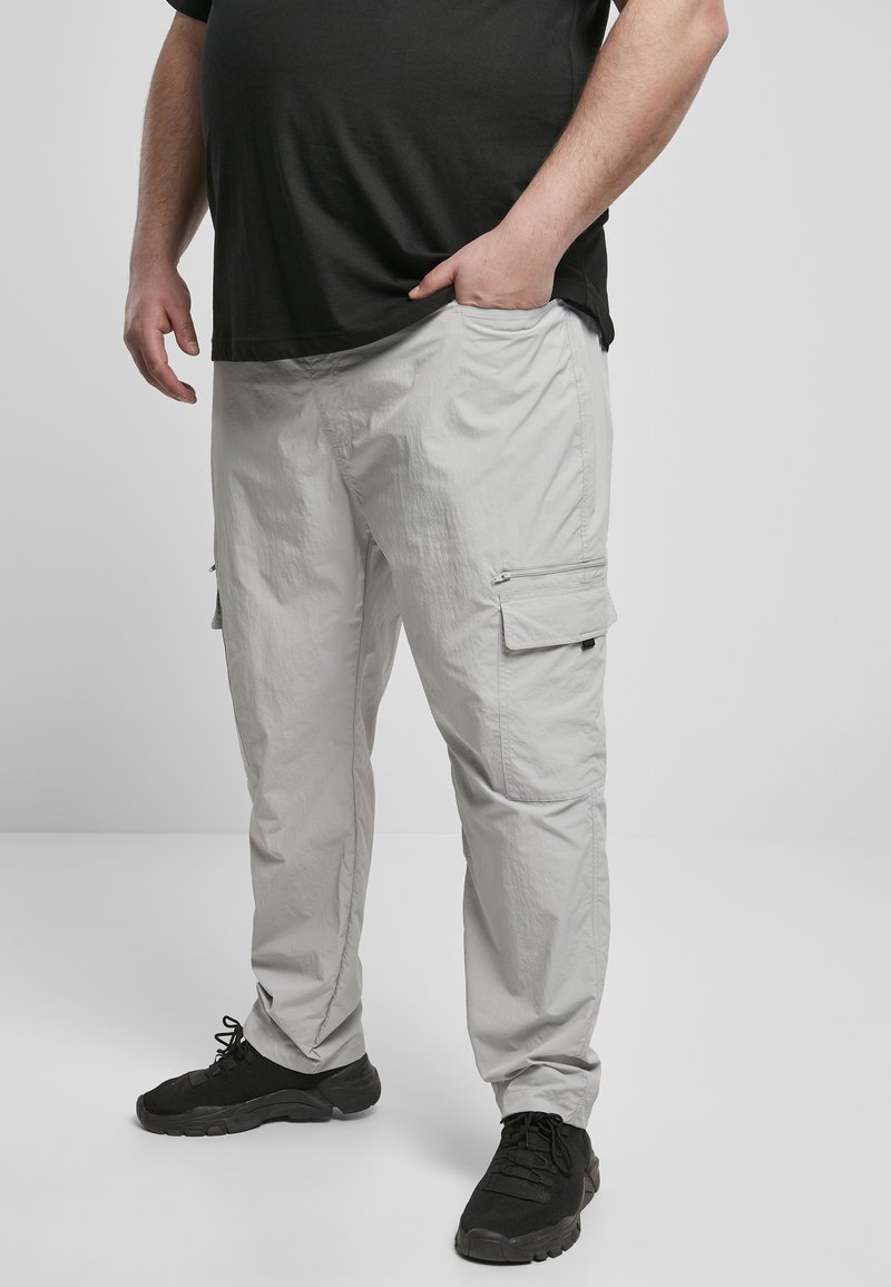 Hellgraue Cargo-Hosen mit entspannter Passform, die Seitentaschen haben und eine Textur aufweisen, die auf ein leichtes, atmungsaktives Gewebe hinweist. Schwarze Sneakers sind getragen.