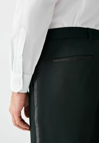 Biała koszula z długim rękawem z zapięciem na guziki, połączona z czarnymi, teksturowanymi spodniami z eleganckim bocznym paskiem i detalem kieszeni z tyłu.