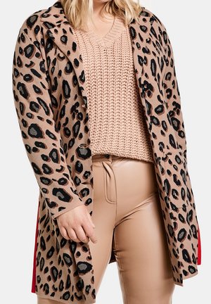 Cardigan con stampa leopardata su base beige, maniche lunghe e colletto. Indossato sopra un maglione rosa a maglia texturizzata e pantaloni beige aderenti.