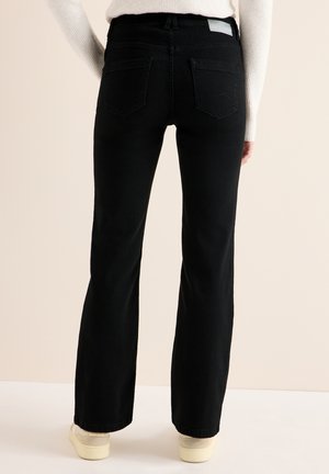Zwarte flared jeans met een gladde textuur, standaard achterzakken en een hoge taille, gecombineerd met lichtgekleurde schoenen.