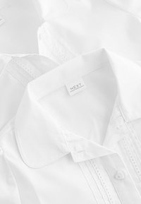 Weißes Hemd mit knöpfbarem Kragen, zarten Nähten entlang der Knopfleiste und einem Etikett mit dem Markennamen "NEXT."