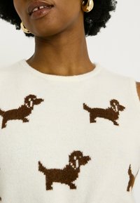 Pull sans manches blanc avec des motifs r épétés de teckels marron. Texture douce avec un col rond et des bords côtelés.