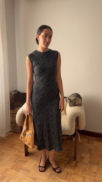 Schwarz mit floralem Muster, ärmelloses Kleid in schlanker Passform, begleitet von einer beigefarbenen Tasche mit runden Akzenten und schwarzen offenen Schuhen.