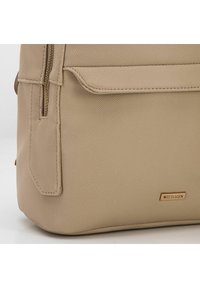 Béžová taška z umělé kůže s texturovaným povrchem, vybavená přední kapsou a zlatými detaily s logem "WITTCHEN".