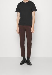 Svart bomulls t-shirt i kombination med slim-fit, mörkbruna byxor. Svarta loafers fulländar looken, mot en enkel vit bakgrund.
