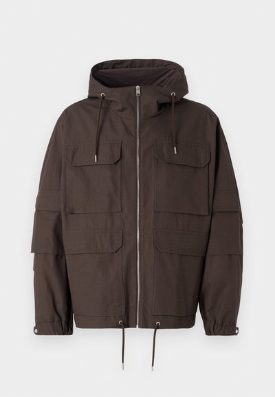 Tumši brūns kapuces džemperis, kas izgatavots no teksturēta auduma, ar priekšējo rāvējslēdzēju, vairākiem priekšējiem kabatām un regulējamām auklām apakšmalā un piedurknēm.