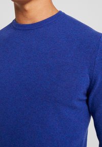 Blå stickad tröja med rund krage, tillverkad av ett mjukt tyg. Texturen verkar slät, med en lätt glans och subtila färgvariationer.