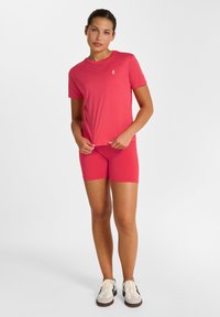 Tæt siddende træningstøj i knaldrød, med en kortærmet top med rund hals og matchende shorts. Blød, glat tekstur.