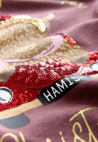 Mørkerød t-shirt med et grafisk motiv af en hamster med røde palietter, guldtekst og en sort label med teksten "HAMISH" under designet.