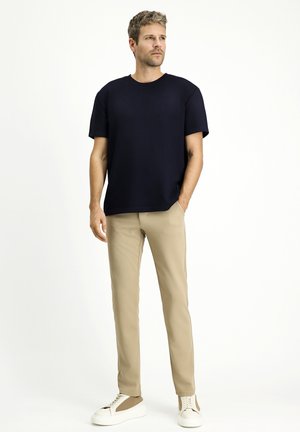 Camiseta de manga corta azul marina combinada con pantalones ajustados beige y zapatillas blancas con detalles marrones. Corte holgado, tela suave y diseño sencillo.