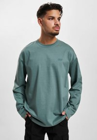 Long-sleeved, cotton-blend shirt in muted teal with a crew neckline and subtle logo detail on the chest.